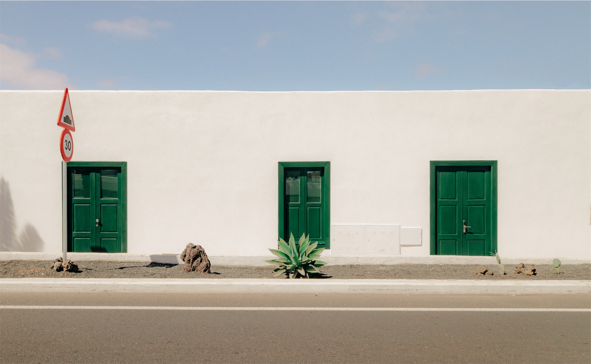 White street facade with green doors and minimal landscaping at Casa Montelogo.