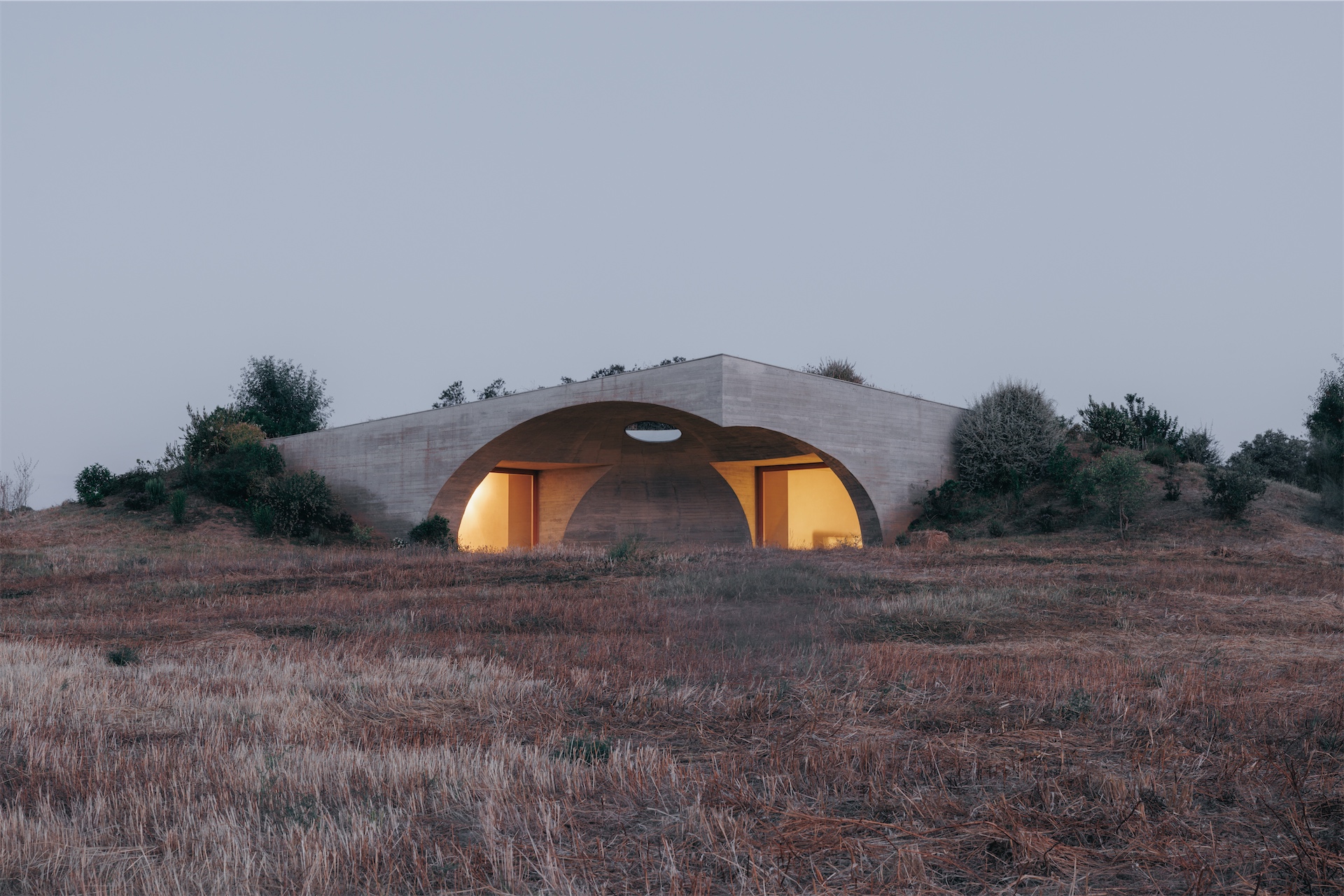 Wide exterior view of Casa na Terra at dusk, set into the landscape.