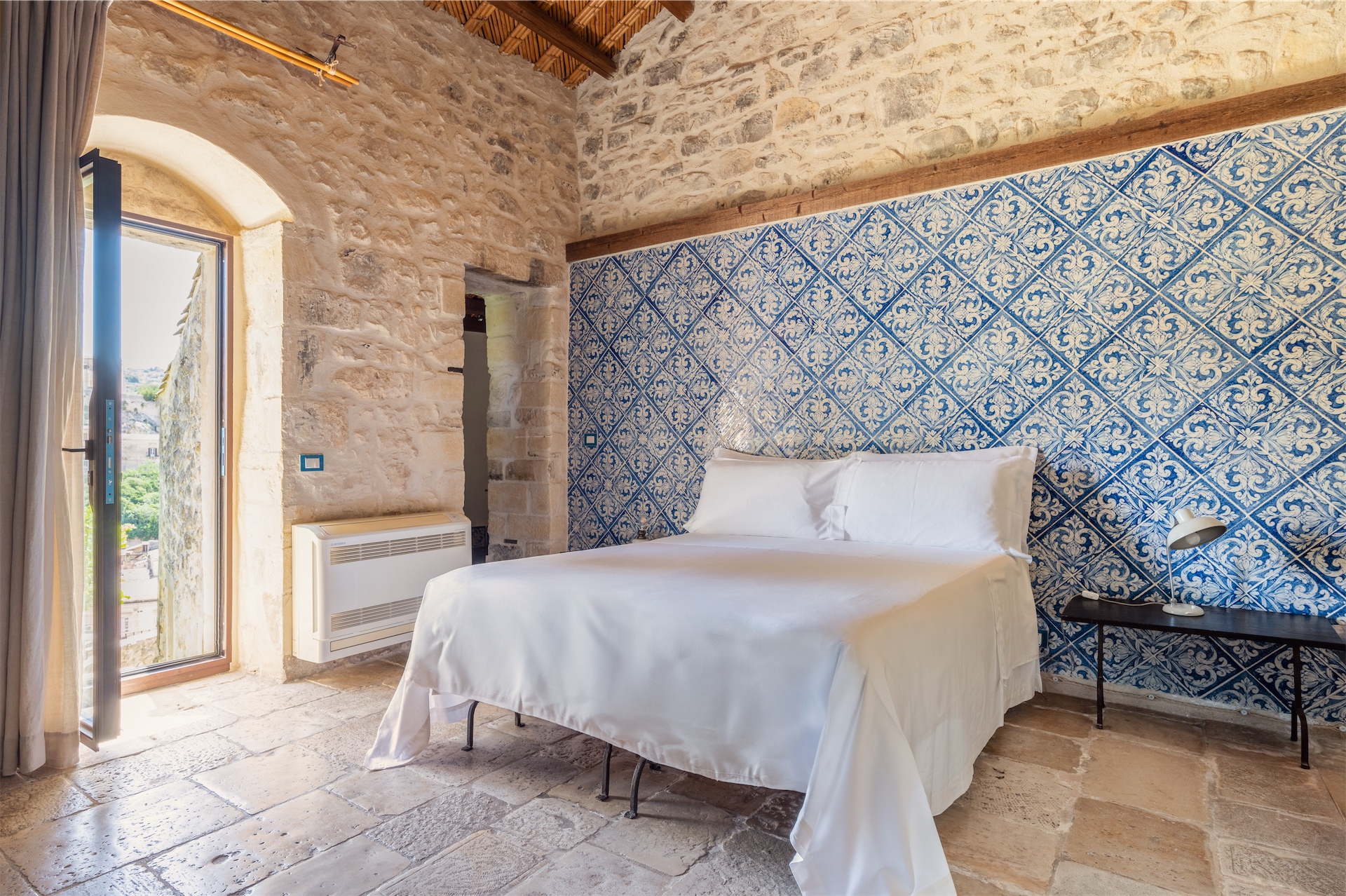Bedroom with blue patterned tiled wall, stone floors, and white bed at Casa Talía.