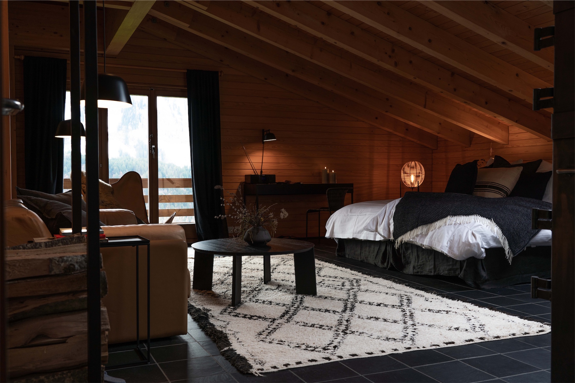 A timber-clad attic bedroom suite with a sitting area and balcony doors at Villa Hundert.
