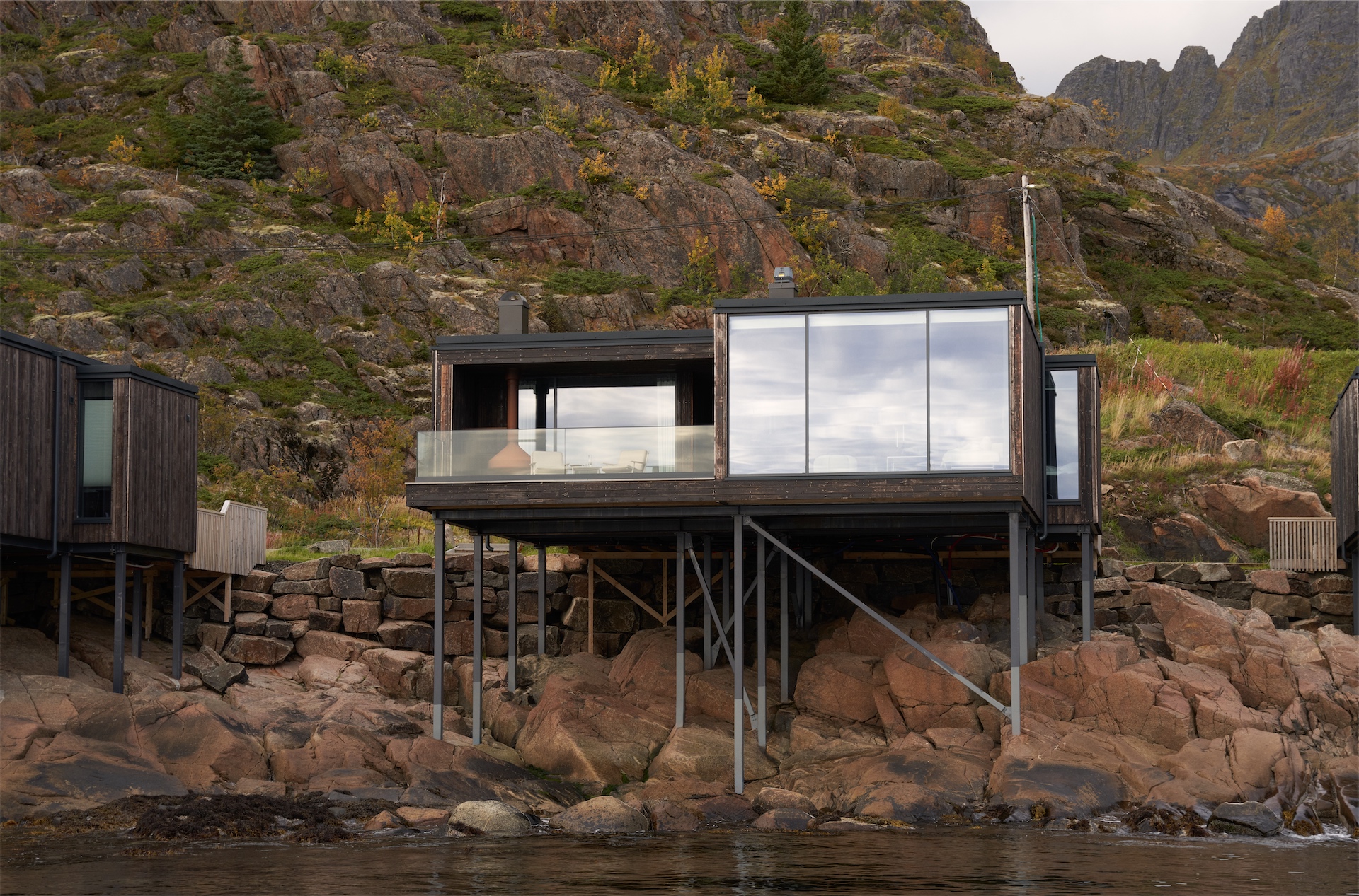 Modern Vipp Lofoten cabin elevated on stilts above rocky shoreline.