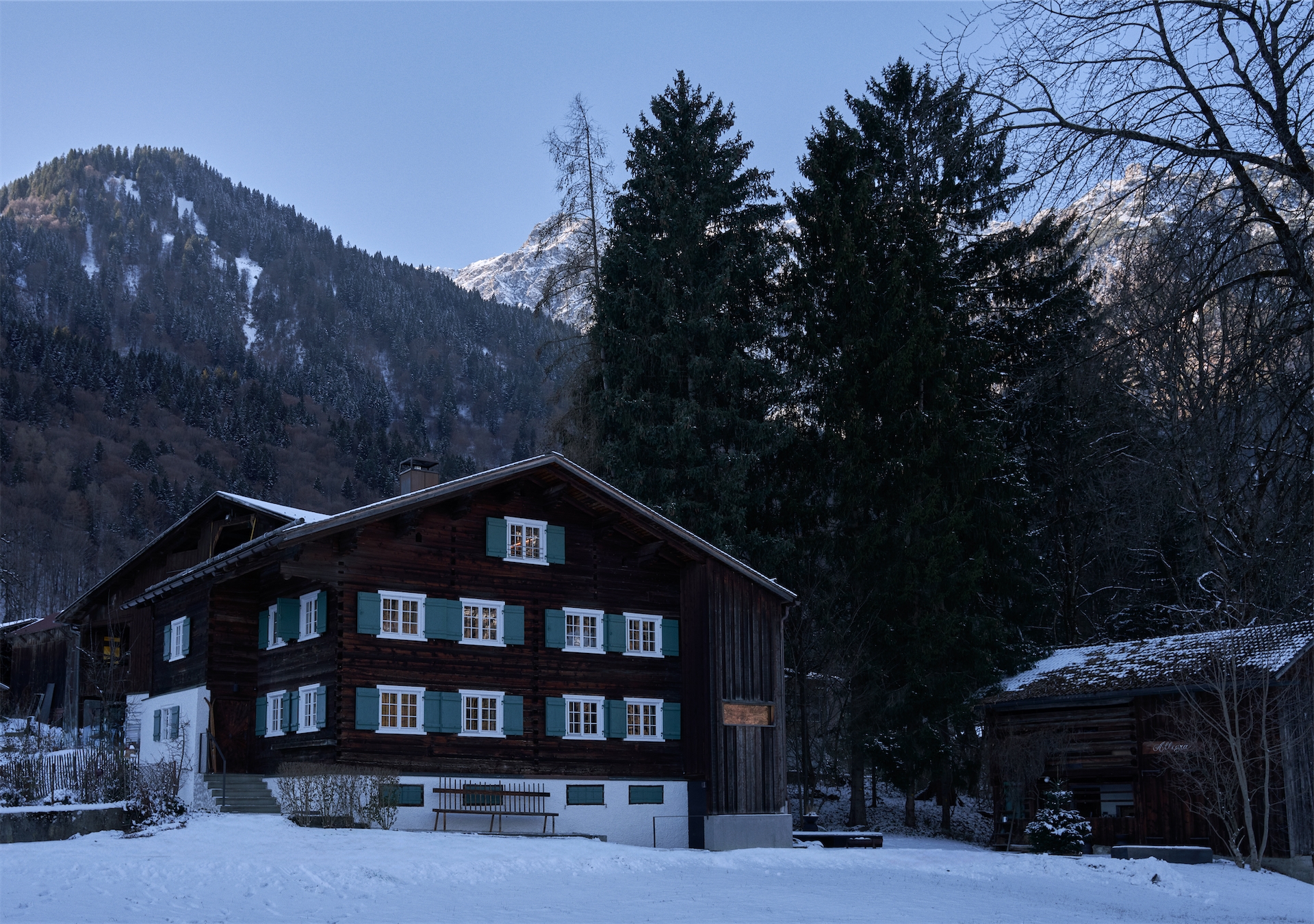 Traditional wooden alpine house with green shutters in snowy landscape.