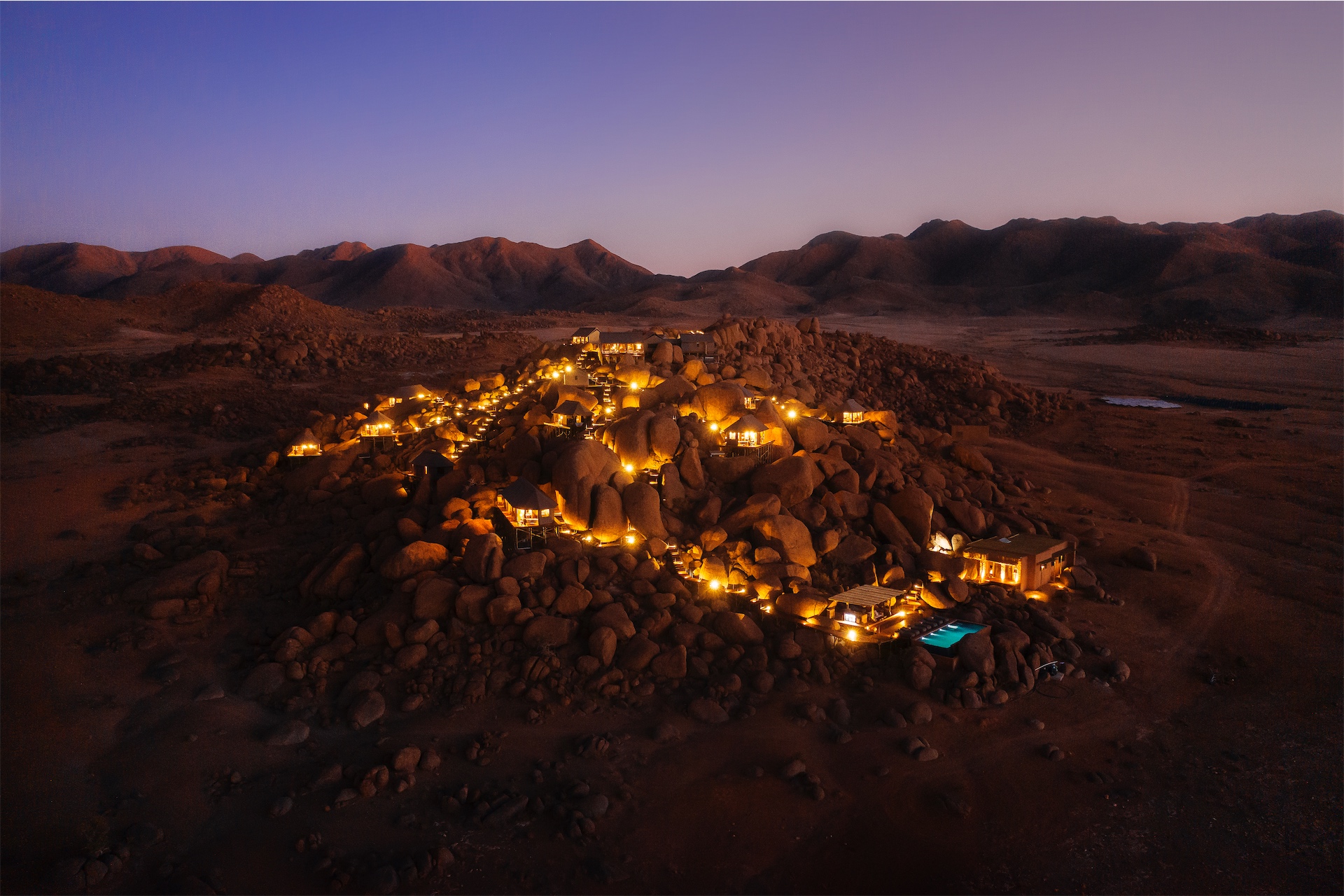 Aerial view of illuminated tented camp among desert boulders at night at Zannier Sonop.