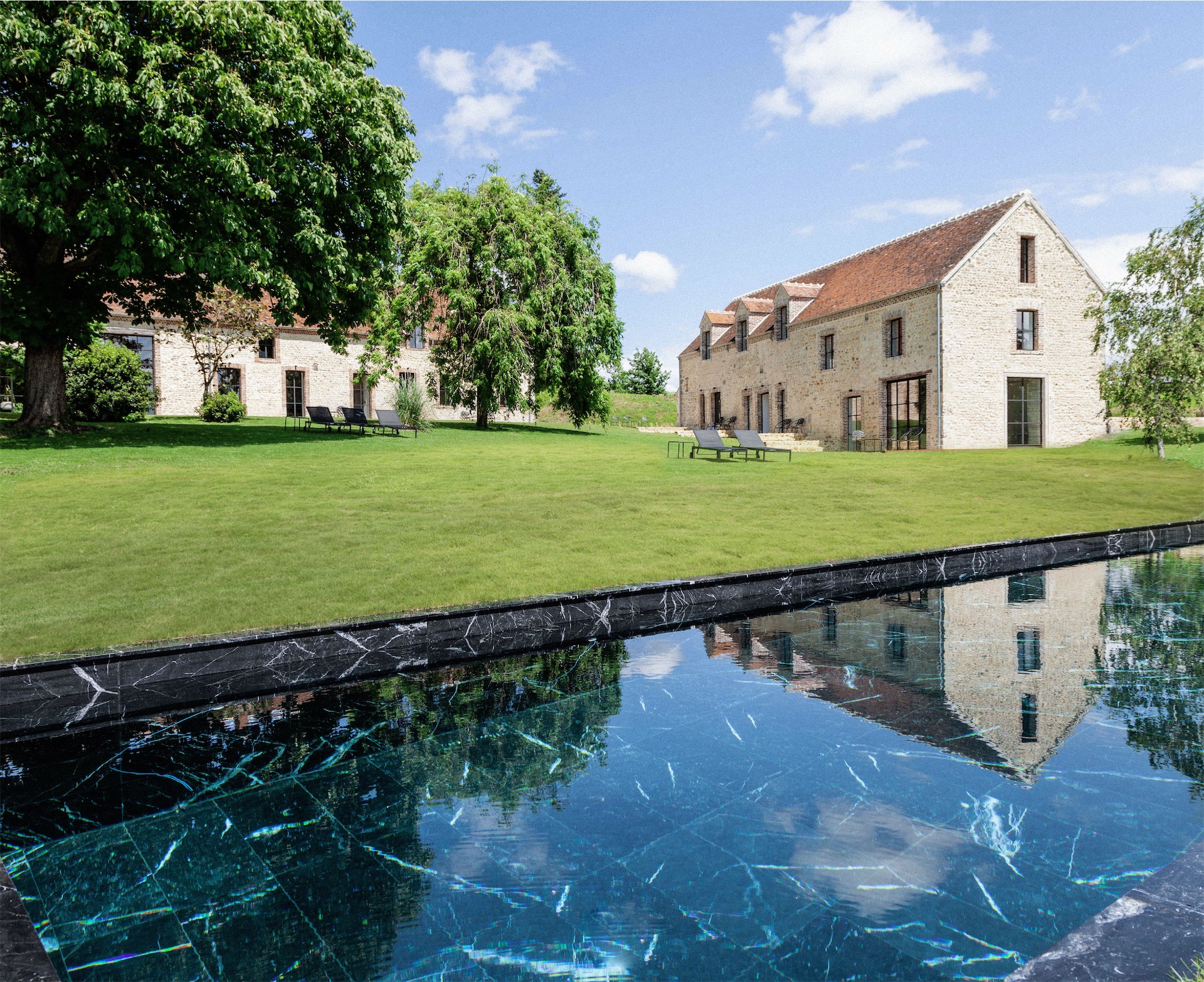 Maison Ceronne exterior: a black marble-edged reflecting pool in foreground, with the stone farmhouse and manicured green lawns under a summer sky.
