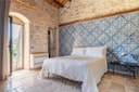 Bedroom with blue patterned tiled wall, stone floors, and white bed at Casa Talía.