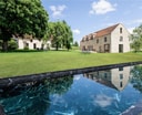 Maison Ceronne exterior: a black marble-edged reflecting pool in foreground, with the stone farmhouse and manicured green lawns under a summer sky.