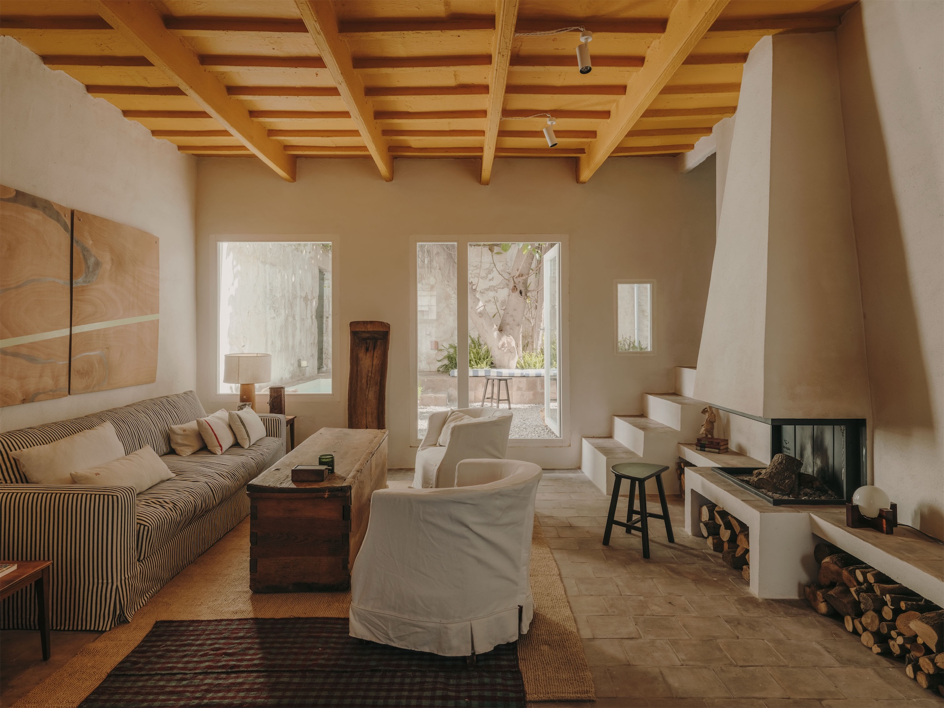 Living room at Bos-Cos Menorca with exposed ceiling beams, fireplace, striped sofa, wooden furniture, and courtyard views.
