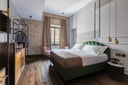 Green velvet bed with brass pendant lights against exposed brick wall.
