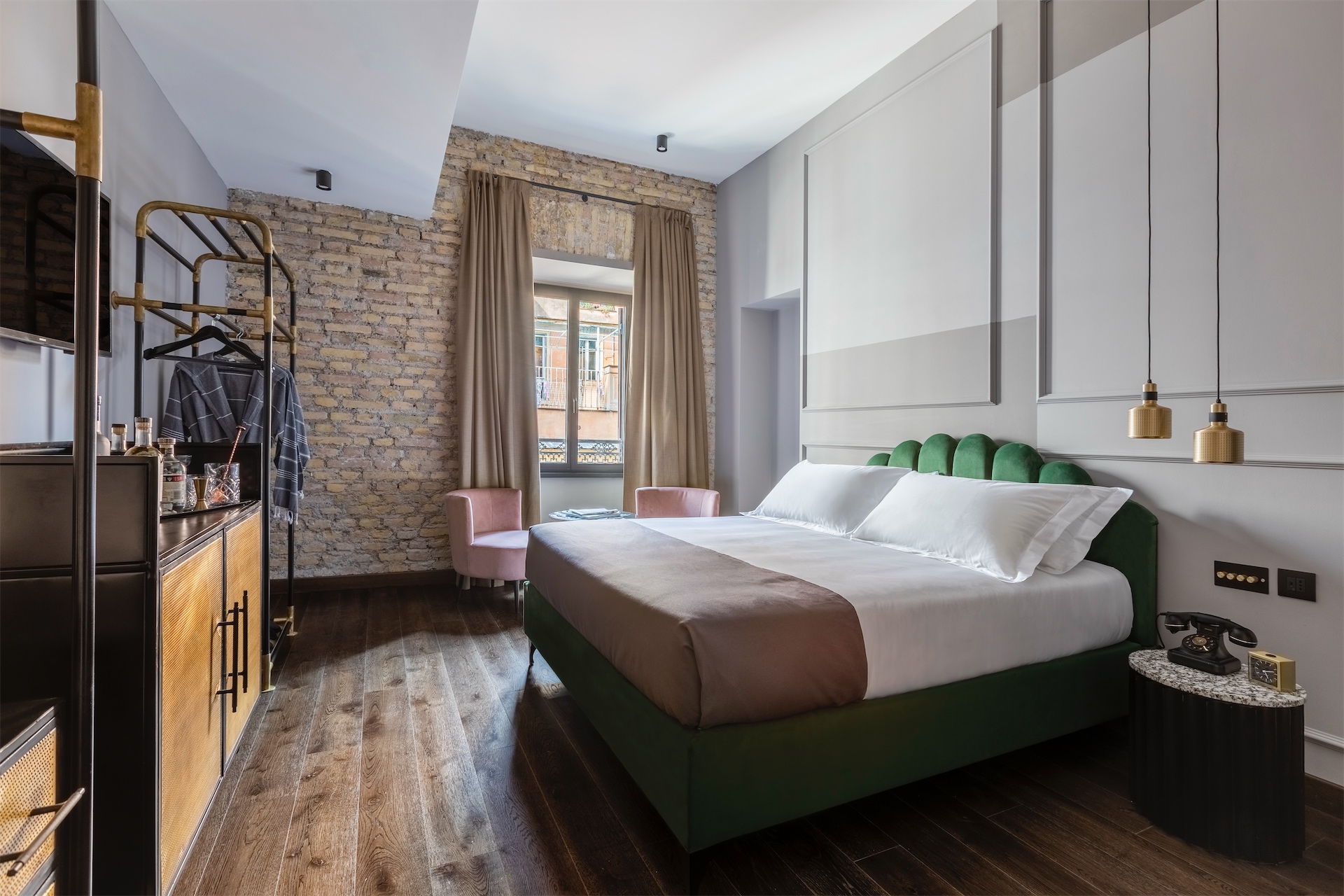 Green velvet bed with brass pendant lights against exposed brick wall.
