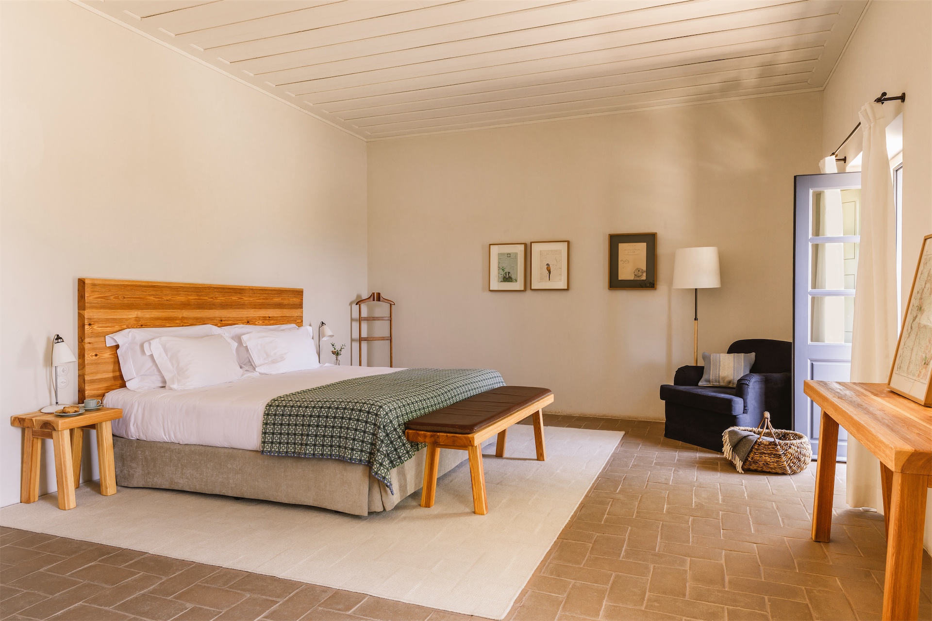 Guest bedroom with wooden headboard, armchair and natural light at São Lourenço do Barrocal.