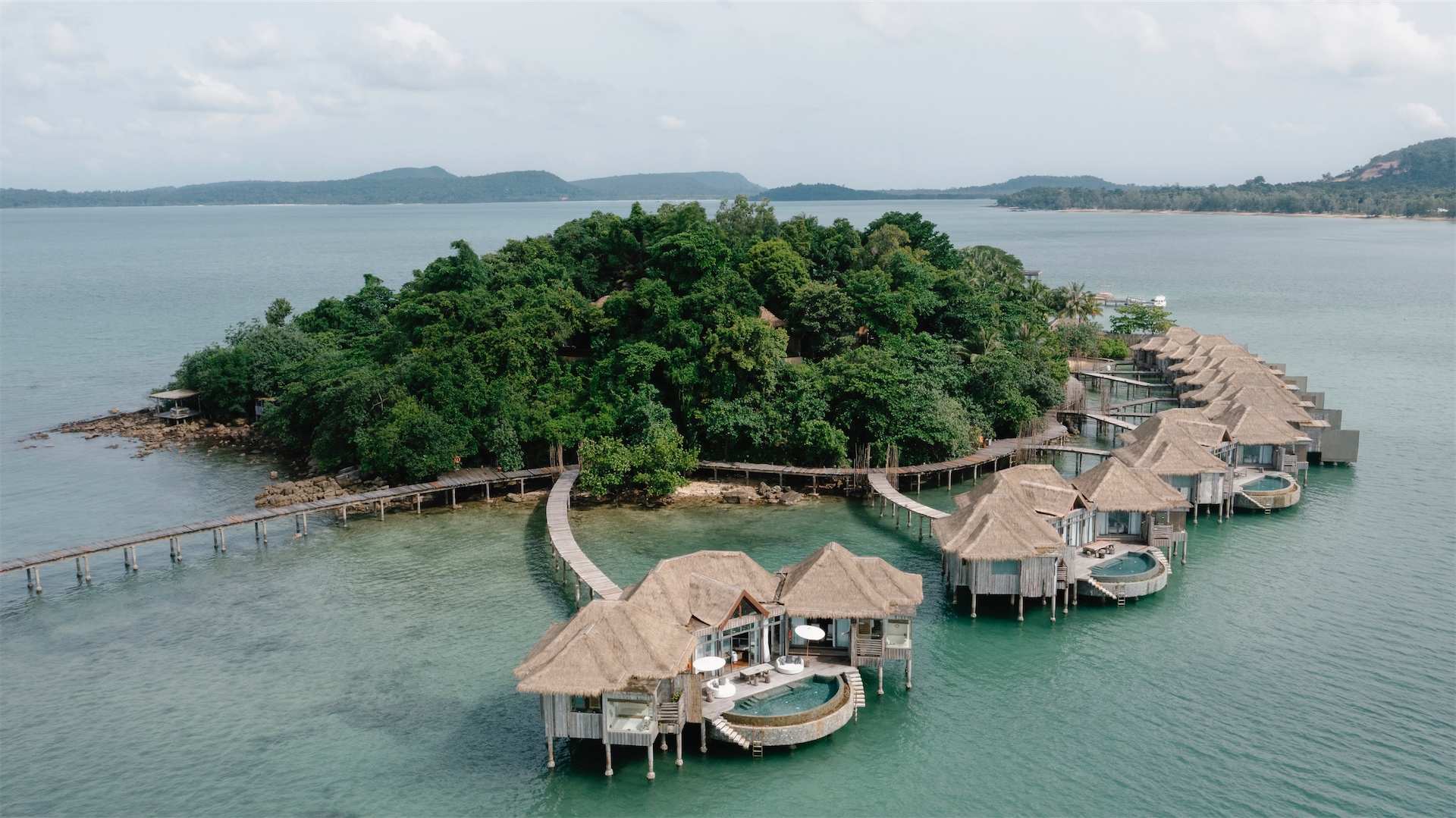 Aerial view of overwater villas connected by curved wooden boardwalk at Song Saa Private Island in Cambodia.