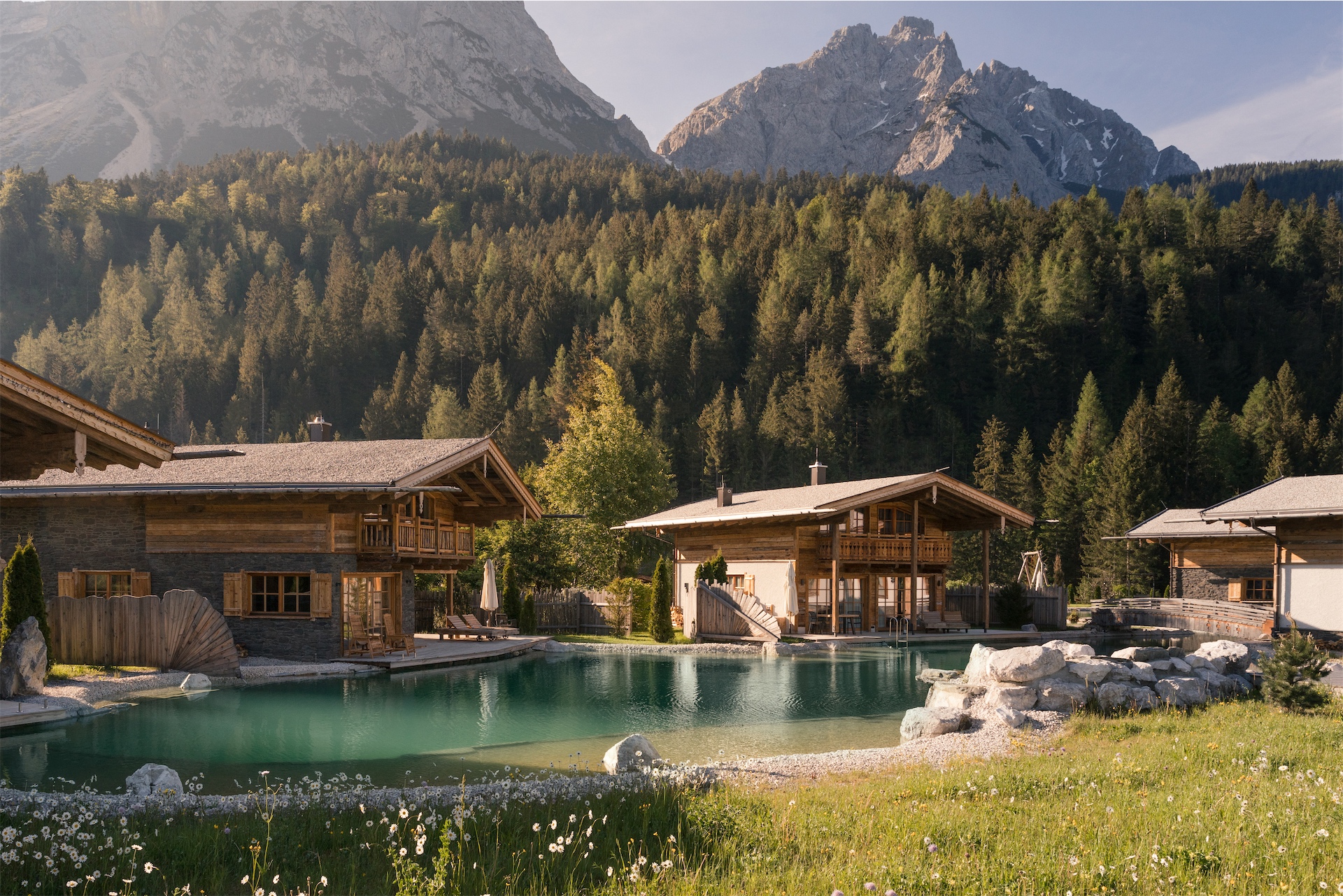 Alpine chalets surrounding a natural swimming pond at LaPosch, set against forested mountains.