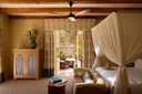 Sterrekopje Farm bedroom with canopy bed, patterned curtains, and French doors opening to a private outdoor bathtub amid lush greenery.