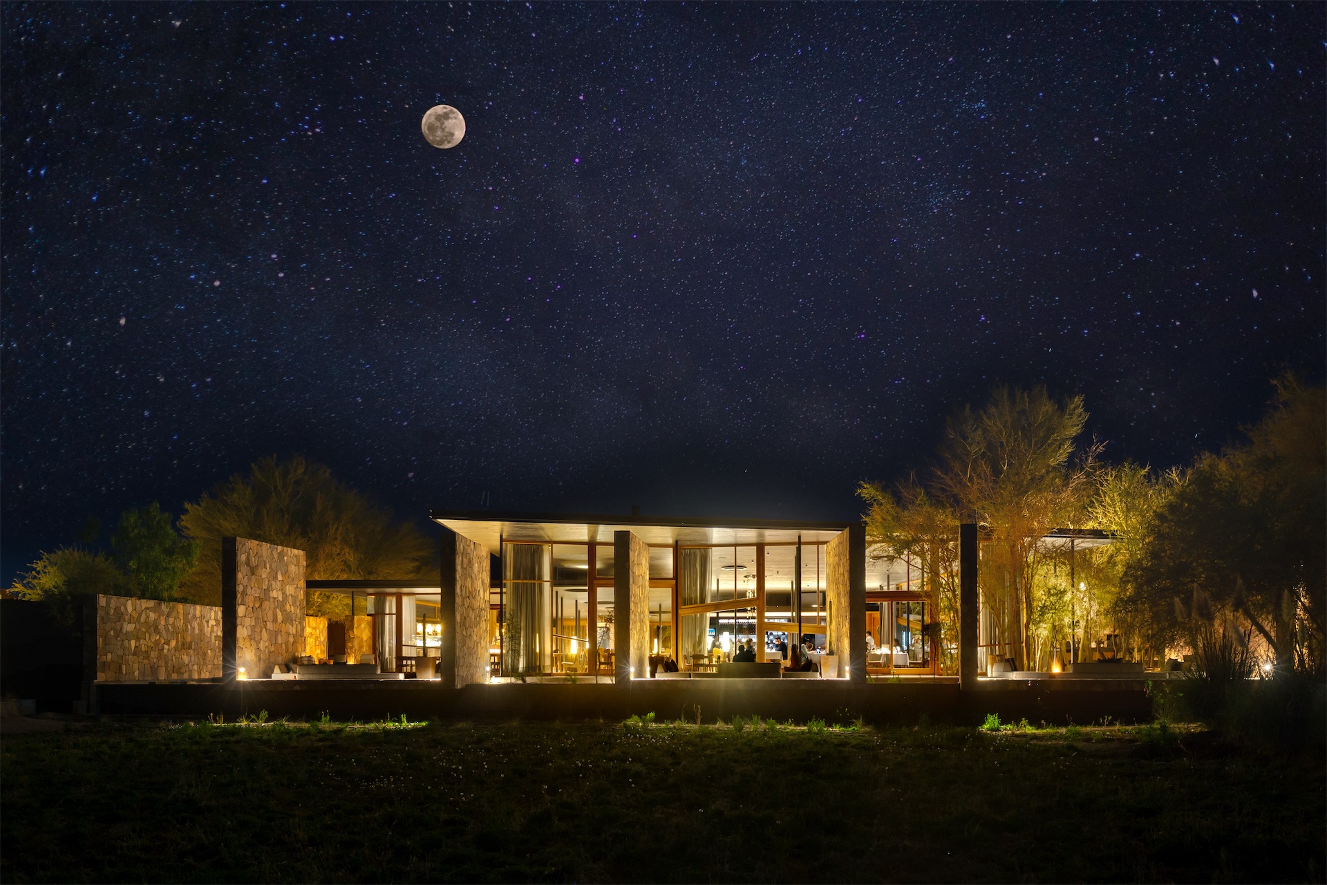 Tierra Atacama lodge lit up at night under a full moon and dense Milky Way star field in the Atacama Desert, Chile